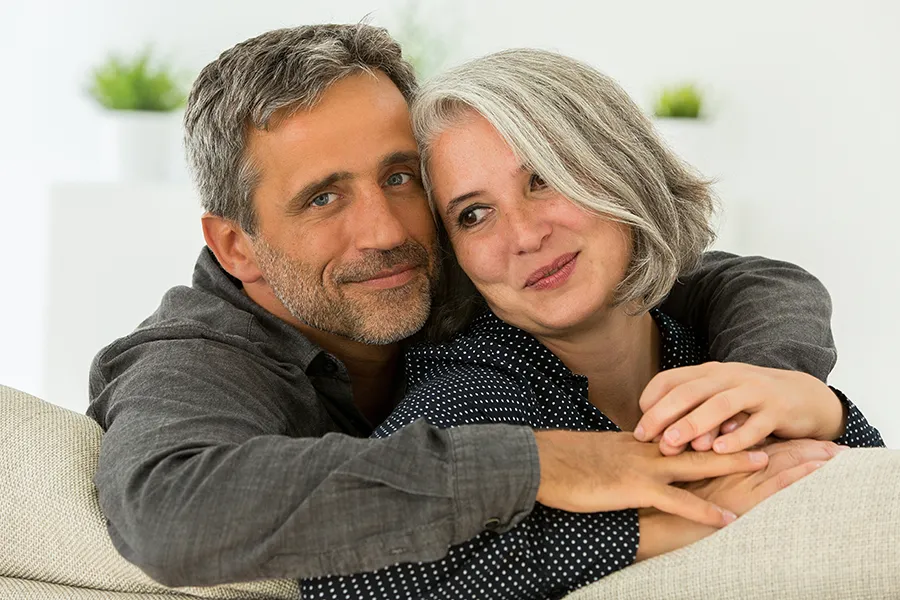 A healthy middle-aged couple happily embracing on their couch. Schedule your consultation with Dr. Bahar Amin to explore the 12-month concierge health program in North York.