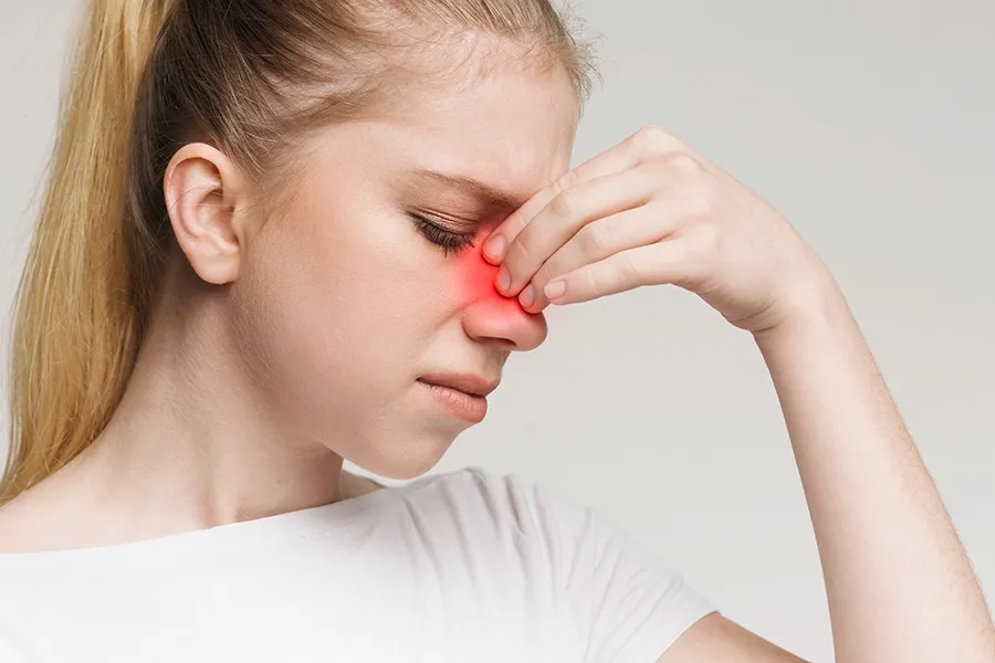 A woman grimaces and rubs the bridge of her nose due to sinus irritation. Get treatment for allergic rhinitis from Dr. Bahar Amin in North York.
