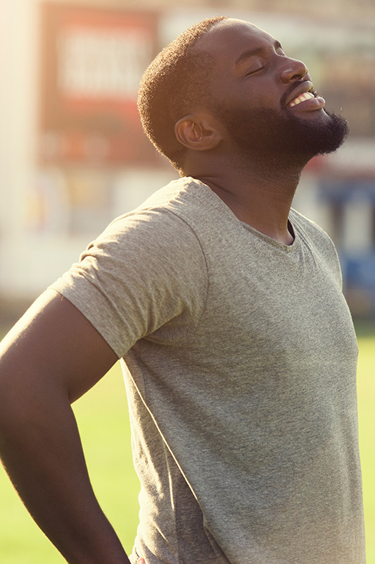 A black man in a t-shirt smiles and raises his face to the sun due to relief from allergies. Get treatment for allergic rhinitis from Dr. Bahar Amin in North York.