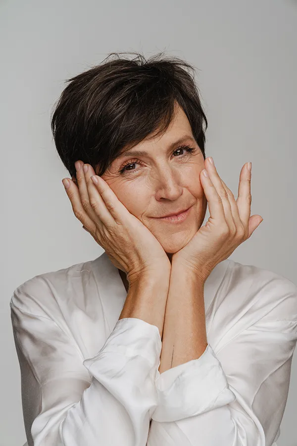 A middle-aged woman with short brown hair touches her face after successful angioedema treatment from Dr. Bahar Amin in North York.