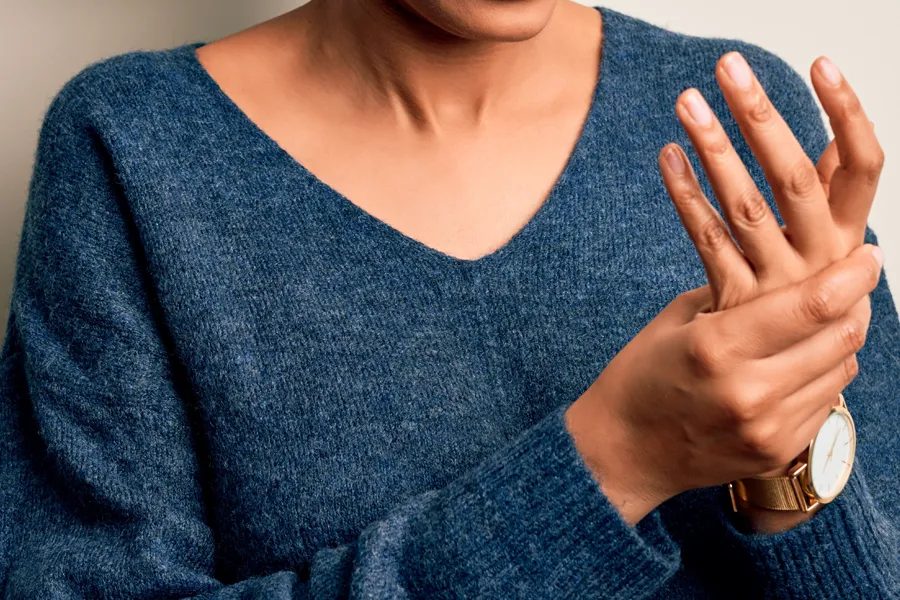 Close up of a woman in a blue sweater massaging one aching hand with the other. Get help for arthritis from Dr. Bahar Amin in North York.