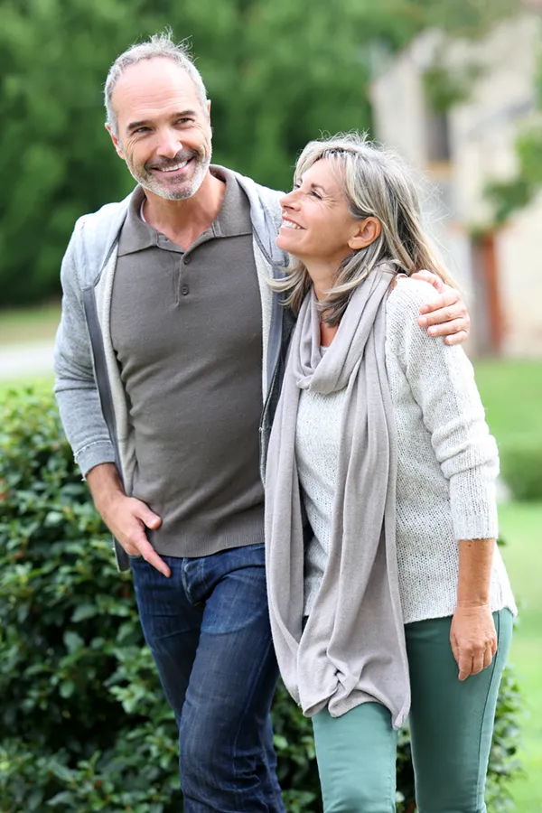 A mature couple in gray toned clothes and jeans walk happily outside, happy with their successful bioidentical hormone treatments from Dr. Bahar Amin in North York.