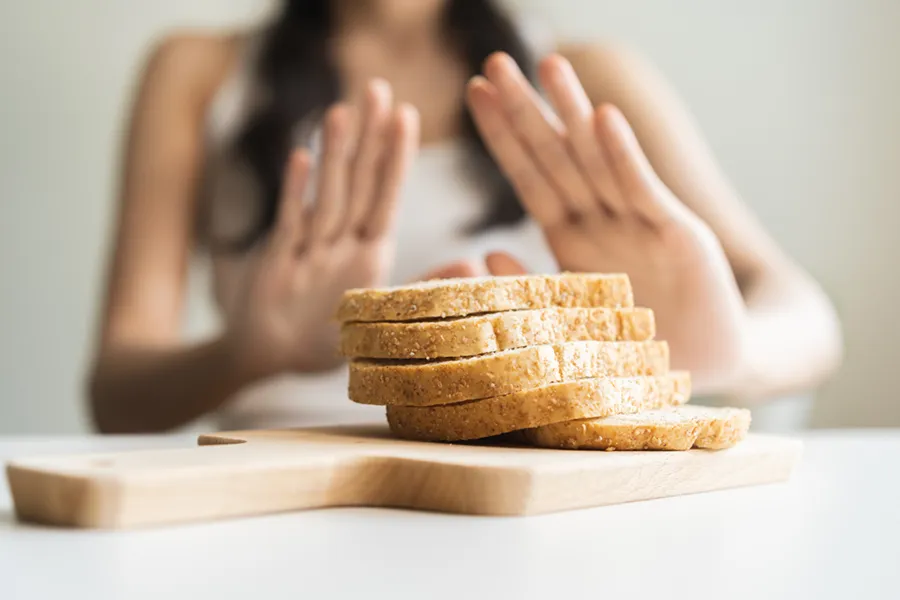 Close up of a stack of bread slices on a cutting board with a woman's hands behind them, refusing to eat. Get treatment for Celiac Disease from Dr. Bahar Amin in North York.