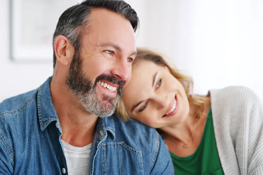 A middle-aged white couple in a bright white room smile and lay their heads on each other. Schedule concierge health and wellness services from Dr. Bahar Amin in North York.