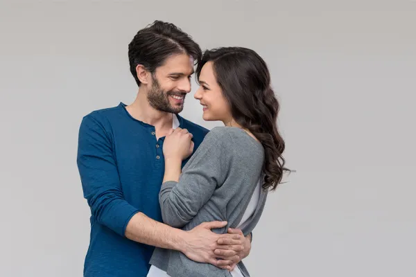 A man in a blue shirt embracing a woman in a gray shirt smiles due to his successful erectile dysfunction care from Dr. Bahar Amin in North York.