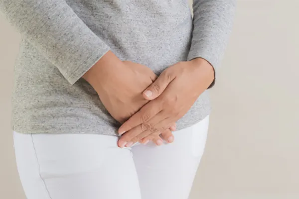 Close up of a woman in a gray shirt and white pants holding her hands below her abdomen in discomfort. Get treatment for fibroids from Dr. Bahar Amin in North York.