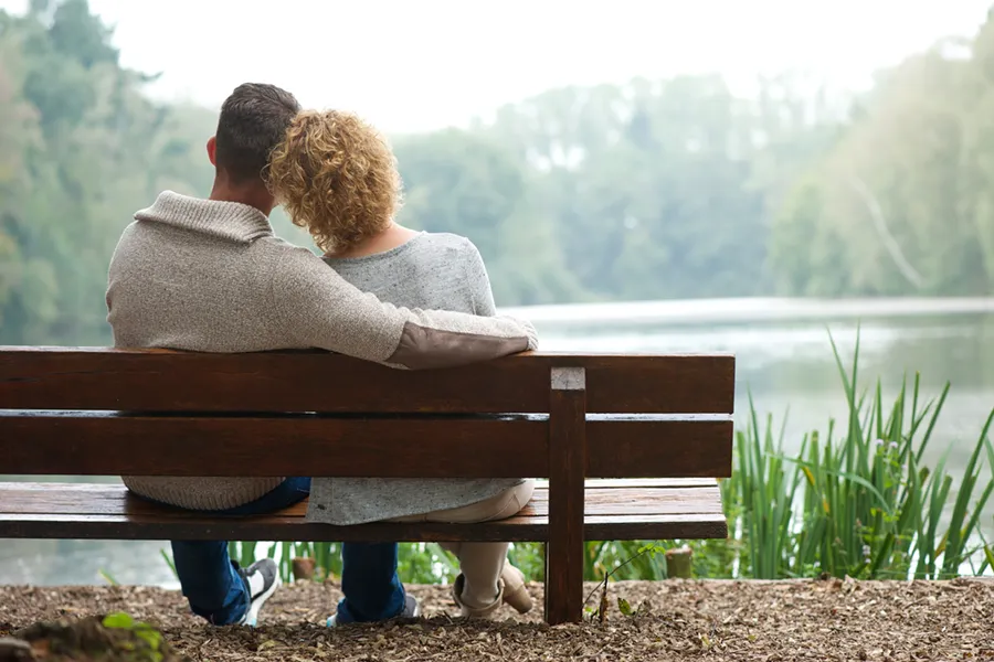 A couple wearing sweaters seen from behind sitting on a bench and looking out at a relaxing lake and forest, representing functional medicine treatment from Dr. Bahar Amin in North York.