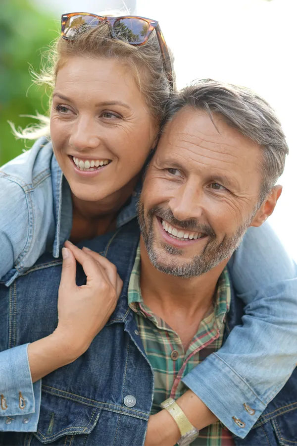 A couple in denim jackets embrace playfully outdoors. Get hypogonadism treatment from Dr. Bahar Amin in North York.