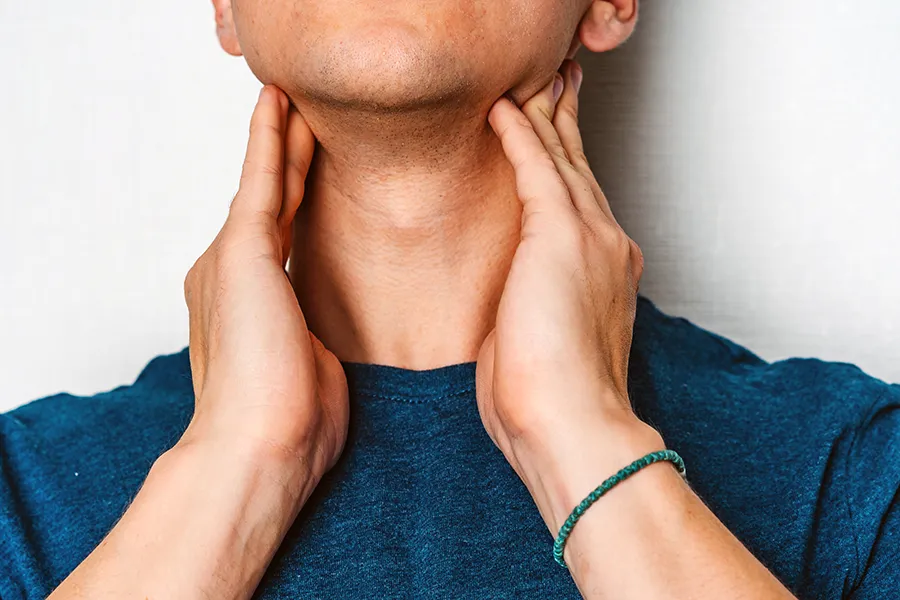 A man in a dark teal shirt rubs the lymph nodes on his neck. Get hypothyroidism treatment from Dr. Bahar Amin in North York.