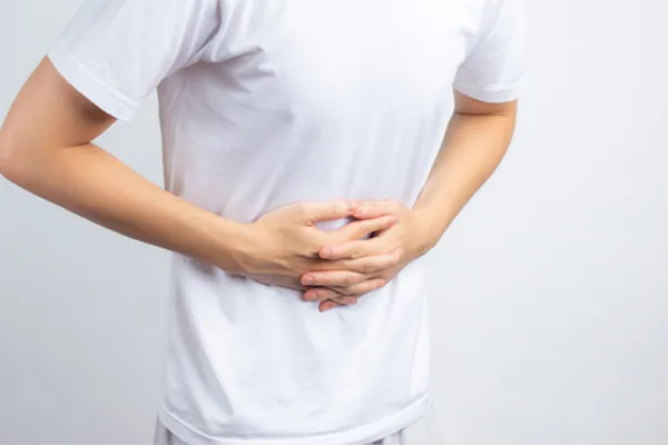 A person holding their stomach in visible discomfort against a plain background. Dr. Bahar Amin treats irritable bowel syndrome with functional medicine in North York.