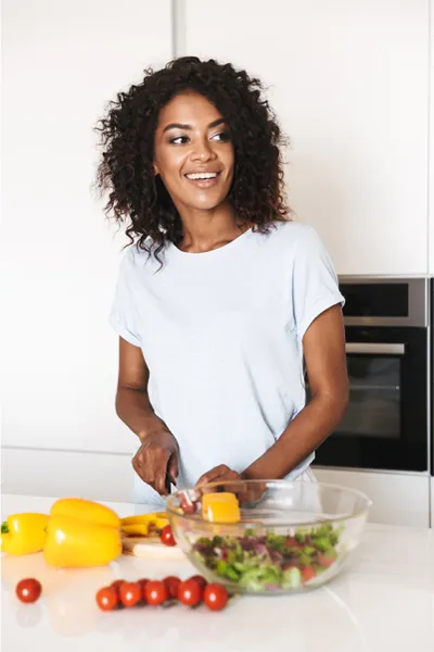 Image featuring a smiling woman chopping vegetables for a salad in a bright, white kitchen. Dr. Bahar Amin offers Irritable Bowel Syndrome Treatment and Digestive Support in North York.