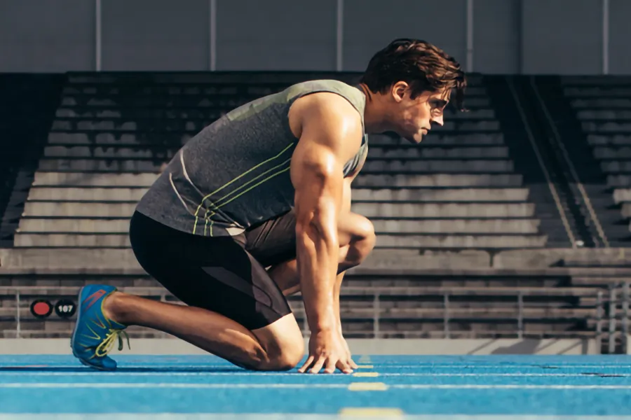 A white man kneels at the starting line on a track, determined to do his best. Get treatment for lean muscle loss and recovery from Dr. Bahar Amin in North York.