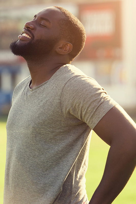 A black man in a gray t-shirt and smiles, looking up with closed eyes after a satisfying workout. Get treatment for lean muscle loss and recovery from Dr. Bahar Amin in North York.