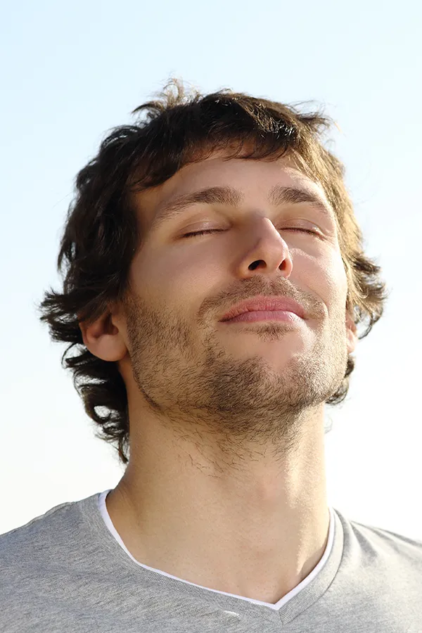 A brown-haired man closes his eyes and breathes in fresh air with his face turned up to the sky. Get treatment for Lupus from Dr. Bahar Amin in North York.