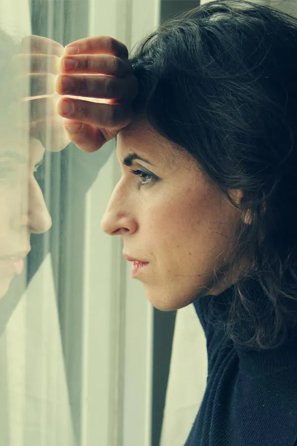 A brunette woman in a thin dark turtleneck looks out the window with a serious expression, suffering from PCOS. Get treatment for Polycistic Ovarian Syndrome/PCOS from Dr. Bahar Amin in North York.