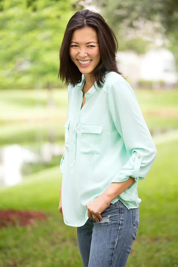 A middle-aged brunette woman in a light green button-up shirt stands outside smiling, happy with her perimenopause treatment from Dr. Bahar Amin in North York.