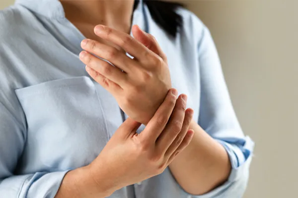 Close up of a woman in a blue blouse rubbing her wrist. Get rheumatoid arthritis treatment from Dr. Bahar Amin in North York.