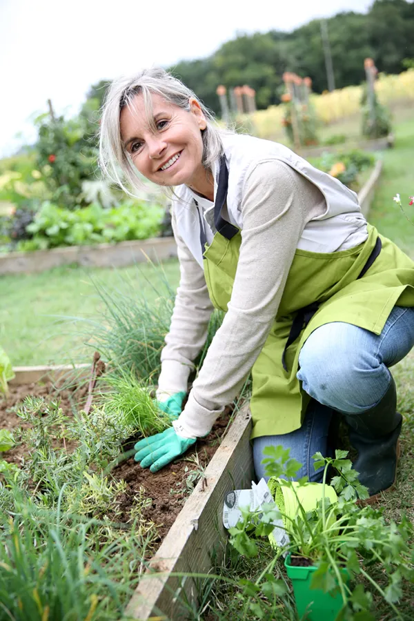 A mature woman bending down working on her garden happily after successful rheumatoid arthritis treatment from Dr. Bahar Amin in North York.