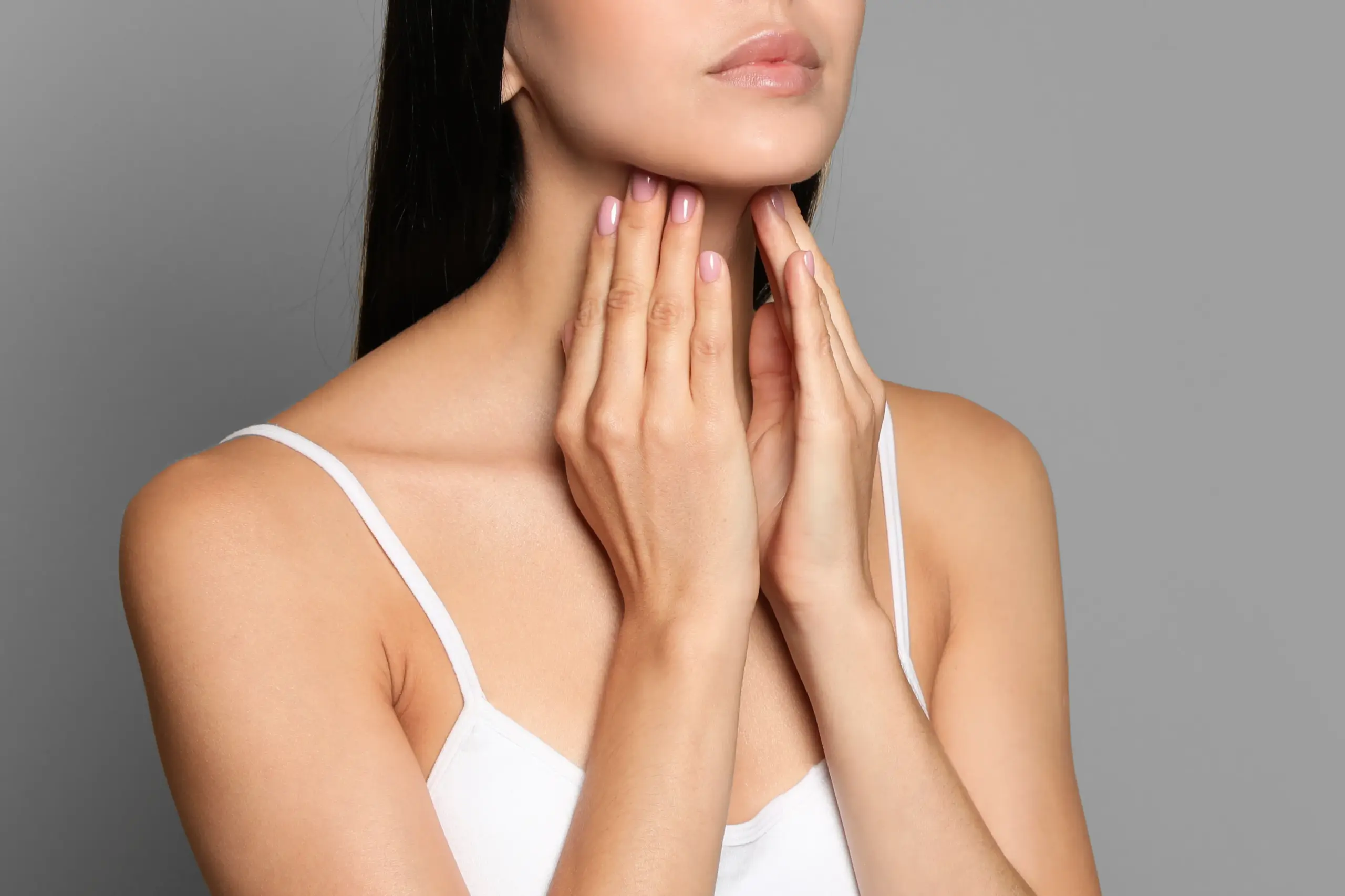 A woman in a white tank top touches her neck looking for signs of thyroid disorder. Get help for thyroid disorders from Dr. Bahar Amin in North York.