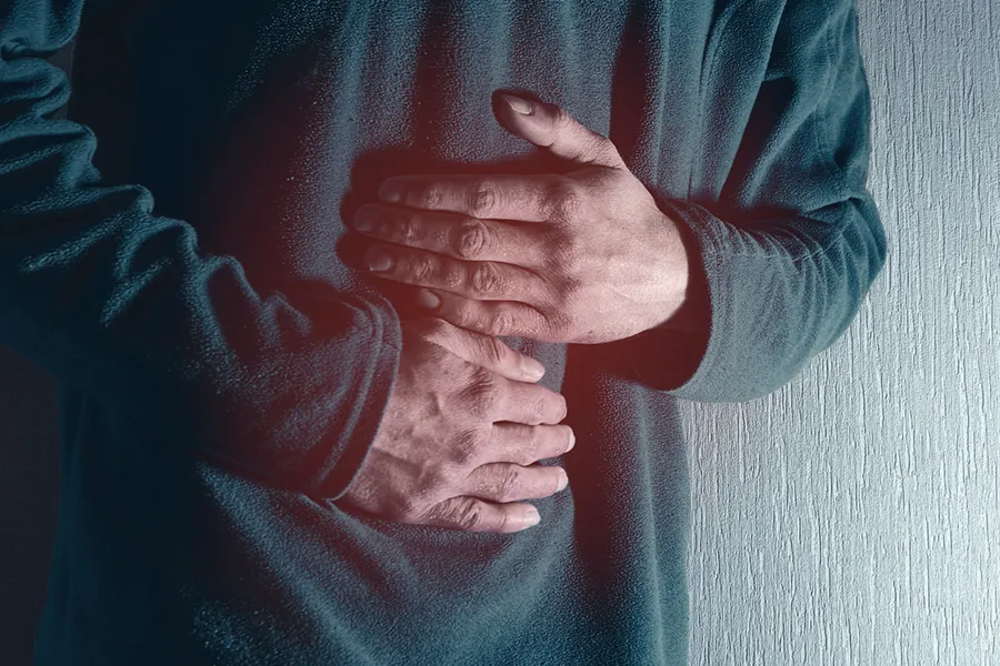 Close-up of the midsection of a man in a green sweater clutching his gut in pain. Get treatment for Ulcerative Colitis from Dr. Bahar Amin in North York.